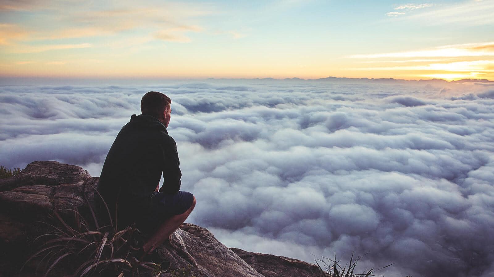 Mann sitzt auf einem Felsen über den Wolken