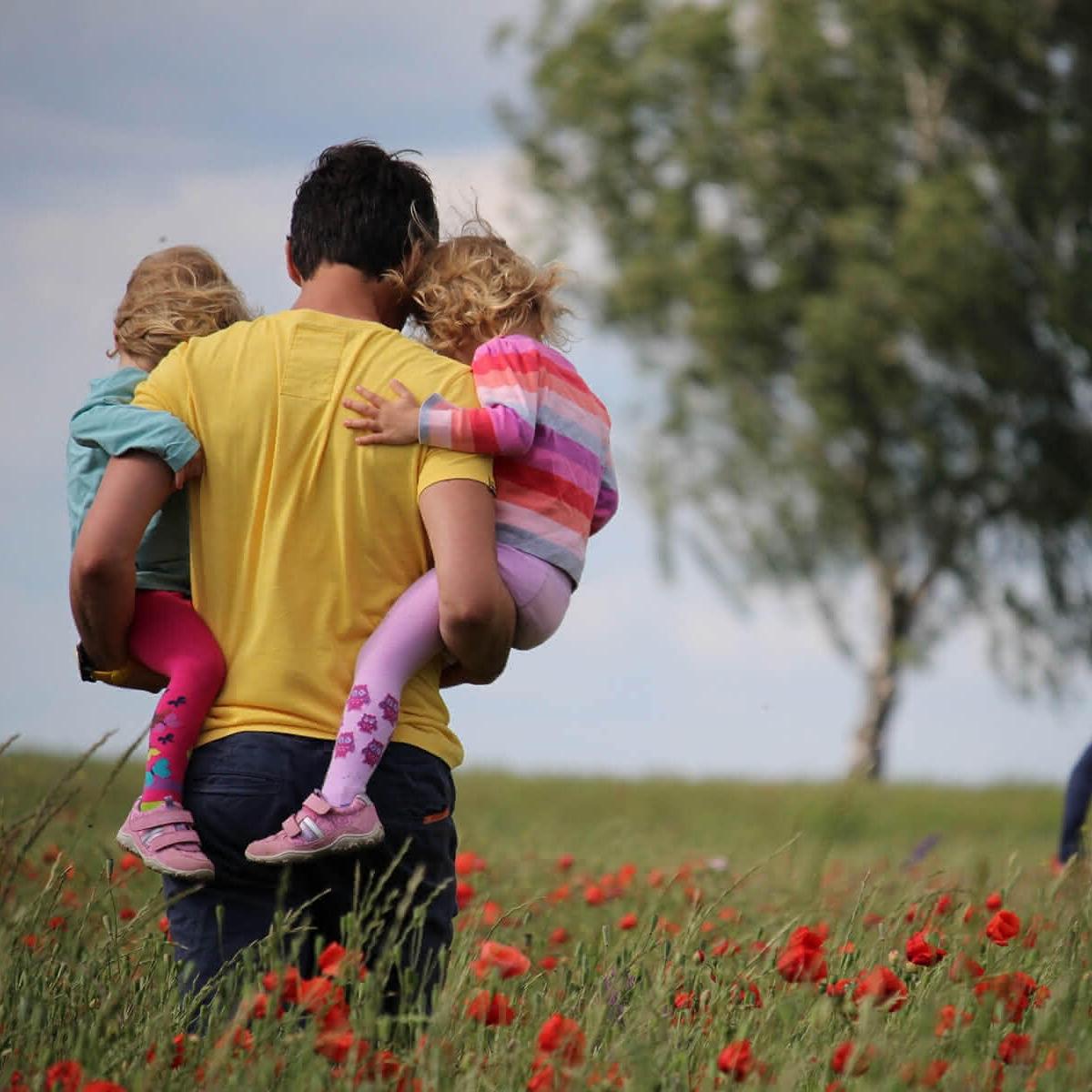 Mann der zwei Kinder in einer Wiese trägt